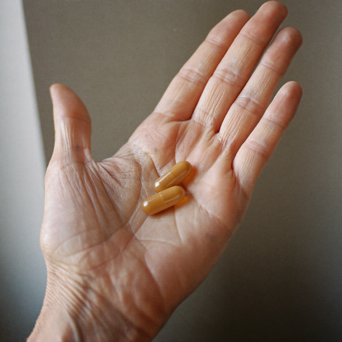 Two amber Enlyven capsules — the daily dose — in an open older hand